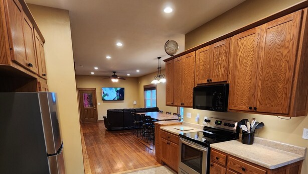 A modern kitchen with wooden cabinets, a stainless steel refrigerator, a microwave, and a dining area with a TV.