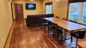A spacious dining area with a wooden table and chairs, a leather sofa, and a television mounted on the wall.