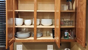 A wooden cabinet with multiple shelves, some holding plates and bowls, and others with jars and a coffee maker.