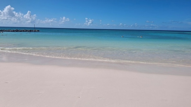 Una spiaggia con acque cristalline turchesi, una riva sabbiosa e alcune persone che nuotano.