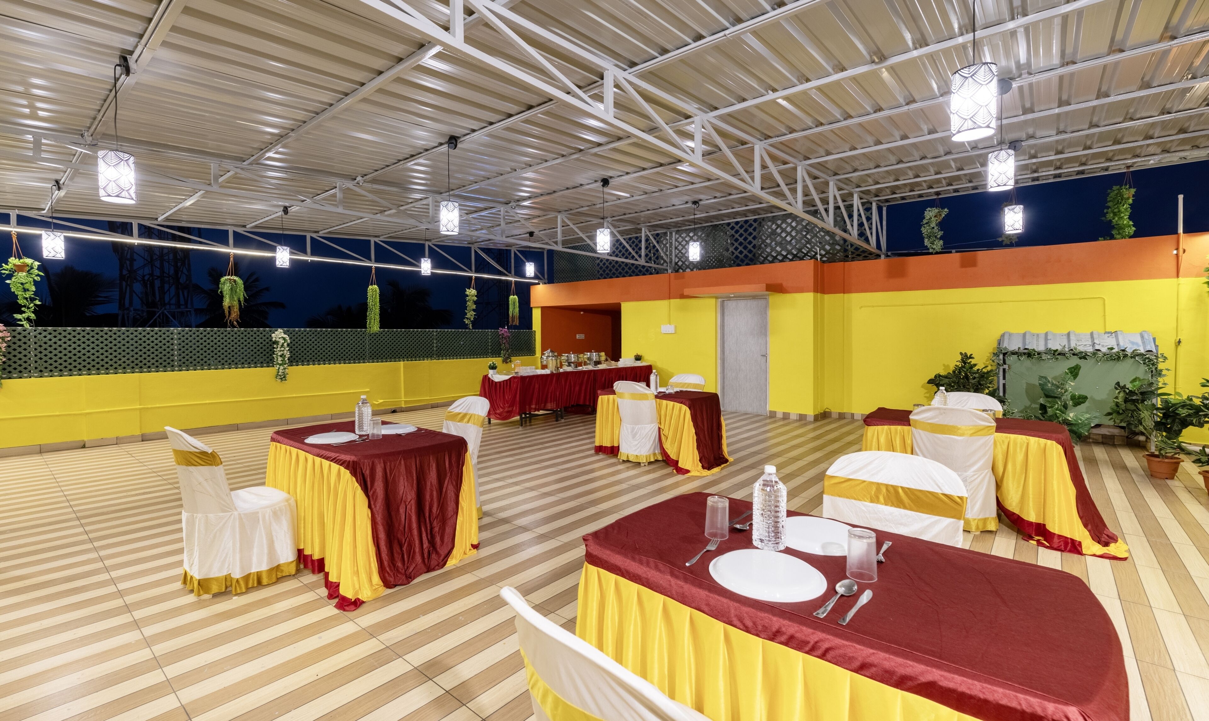 A banquet hall with tables set for dining, featuring a striped floor and a high ceiling with metal beams.
