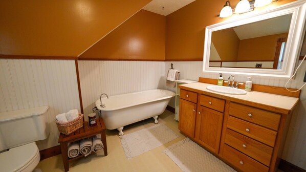 A bathroom with a freestanding bathtub, wooden vanity with a mirror, and a toilet.