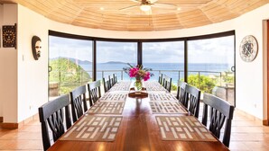 Un espace repas doté d’un plafond en bois, de grandes fenêtres et d’une vue sur la mer.