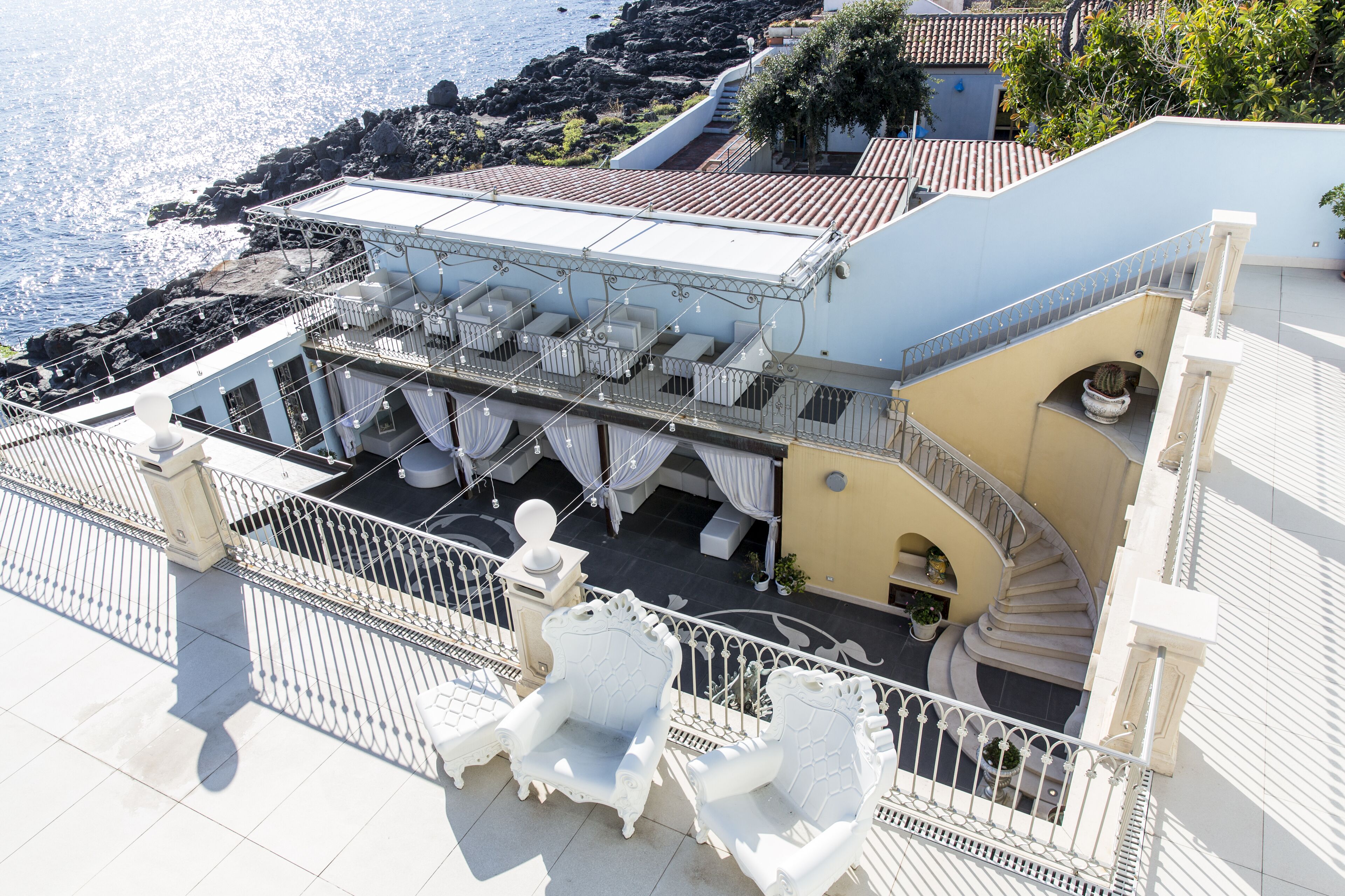 A rooftop terrace with white outdoor furniture, a staircase, and a view of the sea.