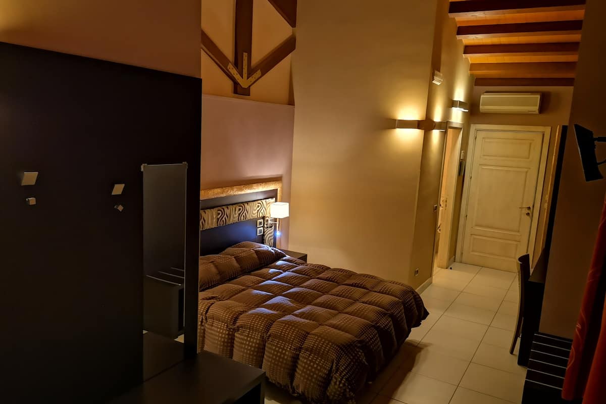 A hotel room with a bed, a desk, and a wardrobe. There is a door and a window in the room.