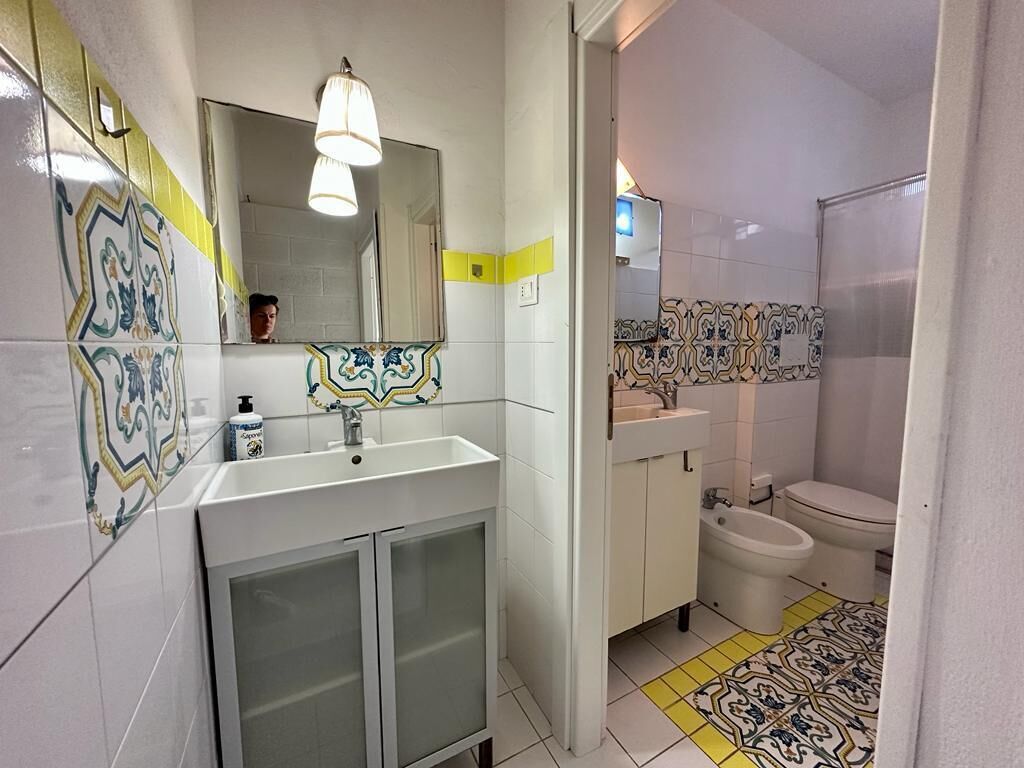 Un baño con un lavamanos blanco, espejo y baldosas estampadas.