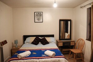 A bedroom with a bed, a desk, a chair, a mirror, and a framed picture on the wall.