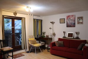 A living room with a red sofa, a yellow chair, a wooden coffee table, and a door leading outside.