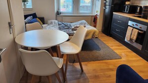 A compact kitchen with a dining area, featuring a white table, chairs, and a bed with a patterned blanket. - Luxury Apartment - Central Dundee - Pet Friendly (Dundee)
