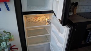 An open refrigerator with empty shelves, a fire extinguisher, and a potted plant on the left. - Luxury Apartment - Central Dundee - Pet Friendly (Dundee)