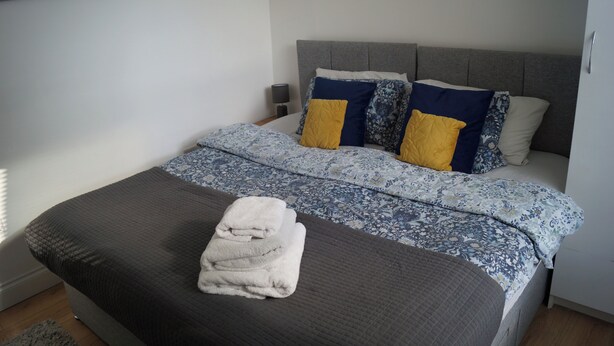 A neatly made bed with a grey headboard, a blue and white patterned duvet, and two pillows, one yellow and one blue. - Luxury Apartment - Central Dundee - Pet Friendly (Dundee)