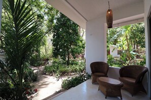 Un área de estar al aire libre cubierta, con mobiliario de mimbre, rodeada de exuberante vegetación y vistas al jardín.