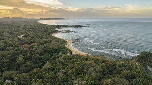 Un paisaje costero con una playa, abundante vegetación y cielo despejado.