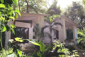 Une maison moderne dotée d’un porche abrité, entourée d’une végétation luxuriante.