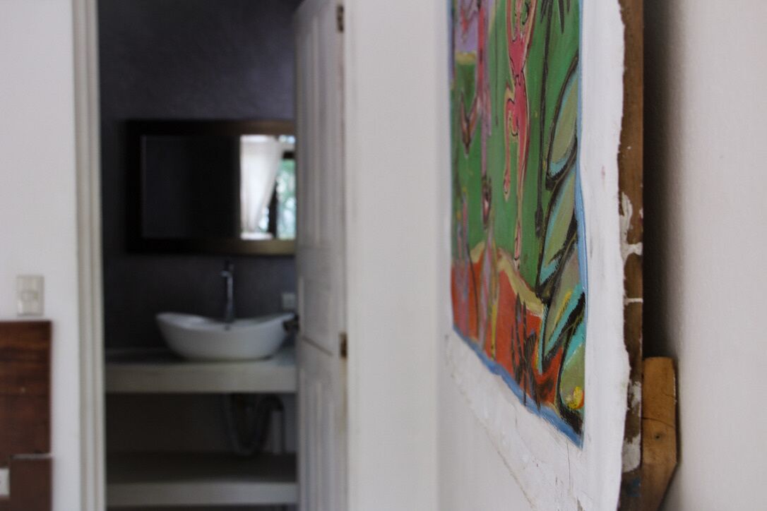 A bathroom with a white sink, a mirror above it, and a colorful abstract painting on the wall.