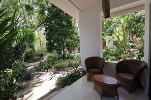 Un espacio al aire libre techado con mobiliario de mimbre, un sendero de hormigón y abundante vegetación.