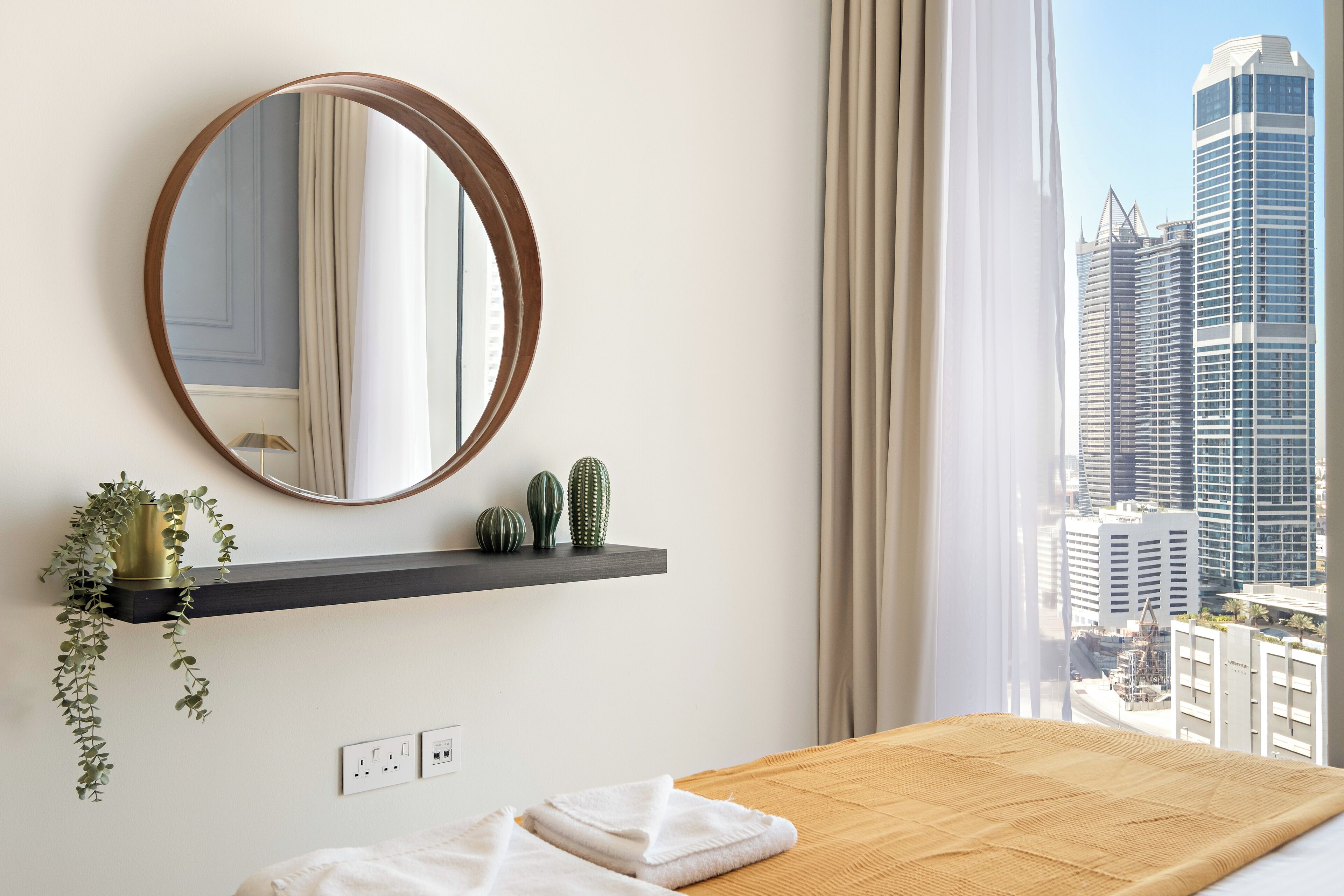 Hotelkamer met een houten bed, een ronde spiegel, een plank met planten en uitzicht over de stad.
