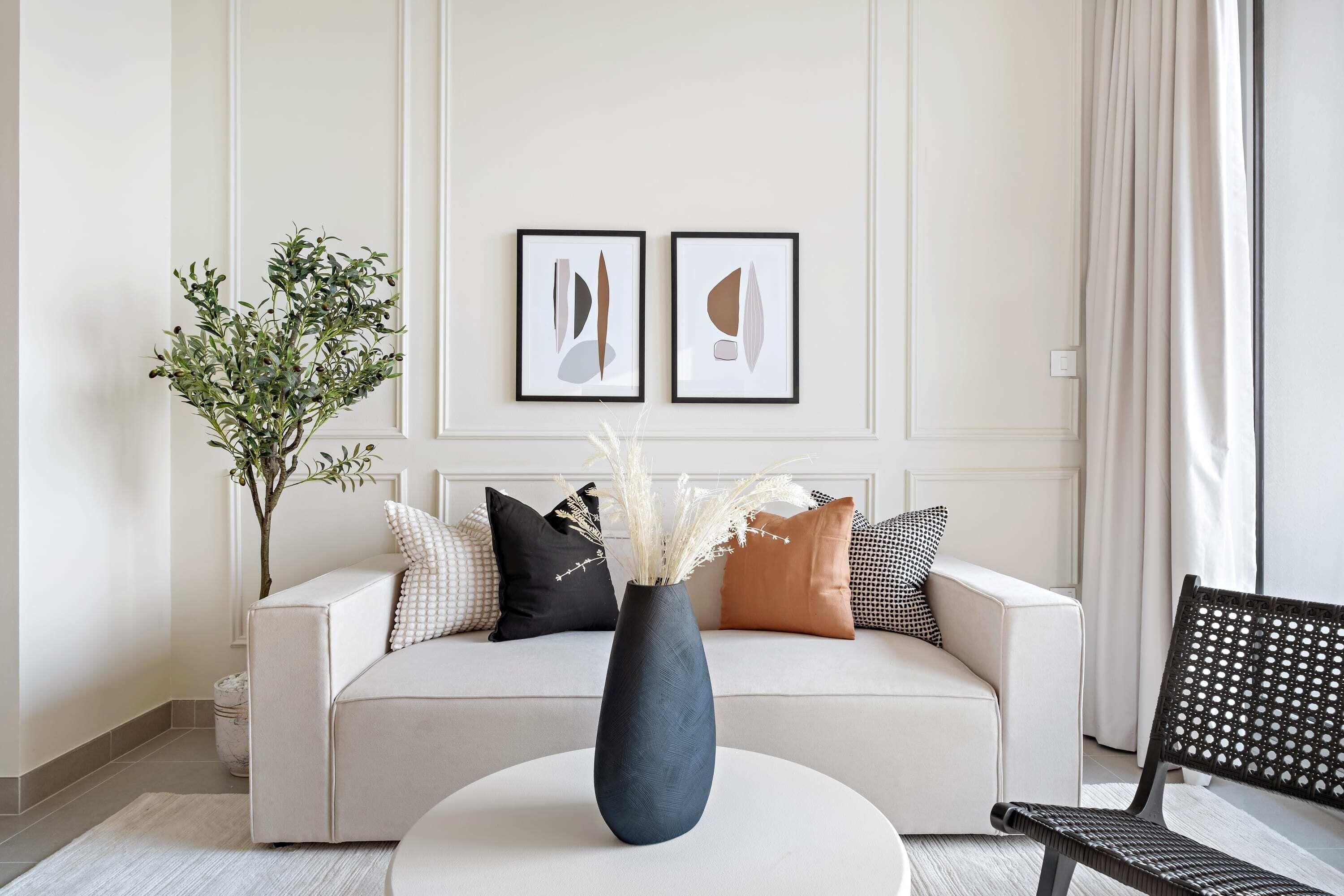 A modern living room with a white sofa, a round coffee table, and a black chair. There is a vase with white flowers on the table.