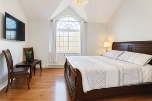 Quarto com cama grande, televisão na parede, escrivaninha com cadeira e janela com cortinas.