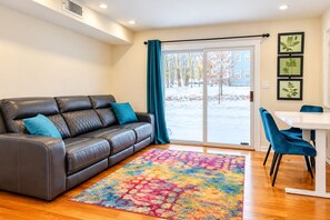 A living room with a leather sofa, a colorful rug, a dining table with blue chairs, and a view of a snowy outdoor area through a glass door. - Newly renovated, first time in the market house with a pool table (Blakeslee)