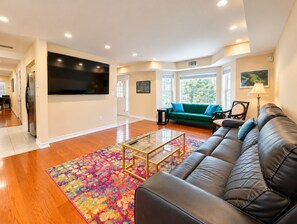 A modern living room with a leather sofa, a colorful rug, and a flat-screen TV mounted on the wall.