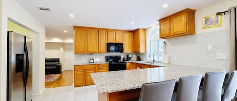A modern kitchen with wooden cabinets, a granite countertop, and a bar area with bar stools.