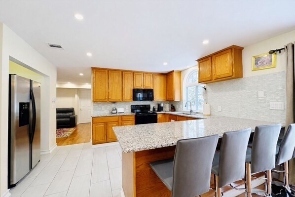 A modern kitchen with wooden cabinets, a granite countertop, and a bar area with bar stools.