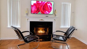 A living room with a fireplace, two leather chairs, a television mounted above the fireplace, and white-framed windows. - Spacious 5BR Poconos Retreat - Sleeps 12 - 3 King Beds - Pool Table- Fireplace (Blakeslee)