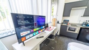 Habitació d'hotel moderna amb un televisor de pantalla plana gran, un escriptori amb un ordinador portàtil, una cuineta petita i un llit.