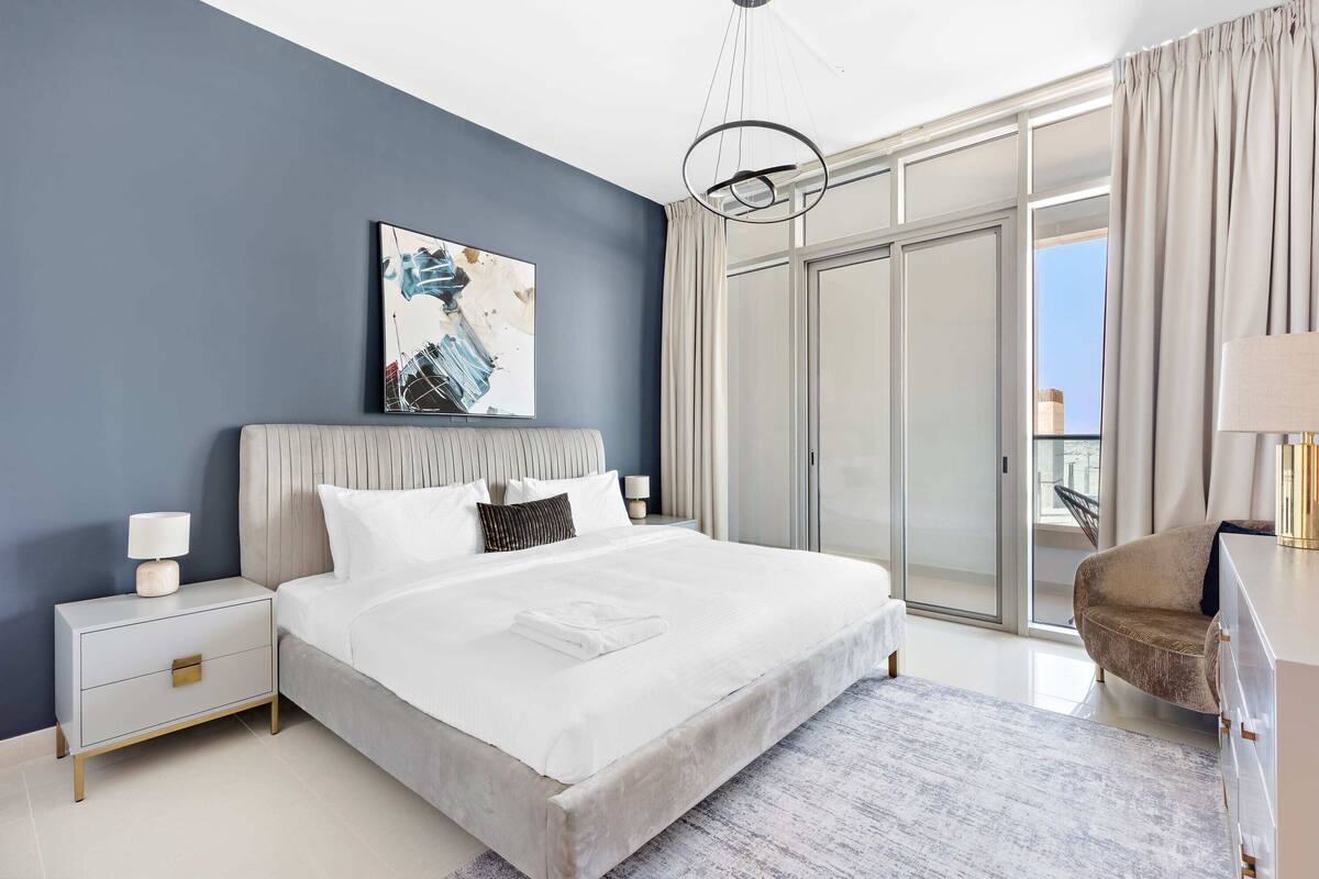 Une chambre moderne avec un grand lit, une table de chevet, une chaise et une porte-fenêtre coulissante donnant sur un balcon.