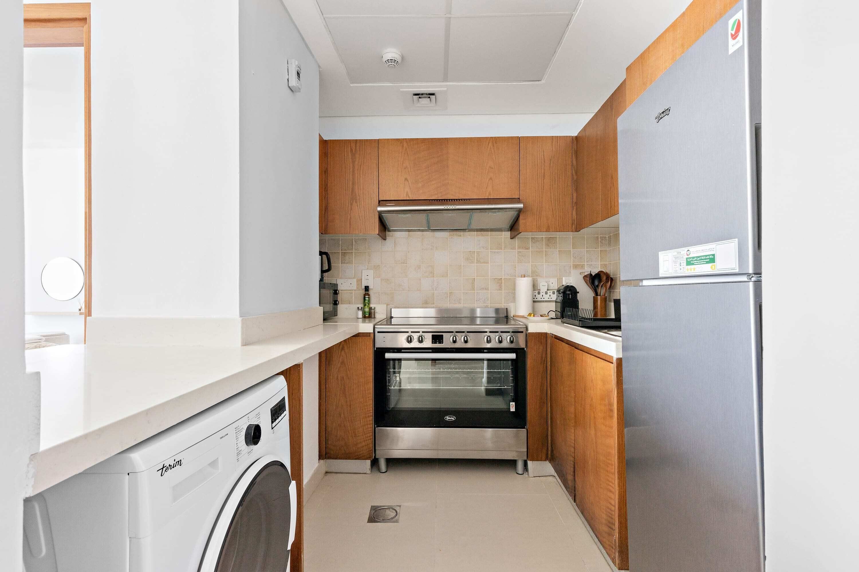 Eine kleine Küche mit Waschmaschine, Backofen und Edelstahlkühlschrank.