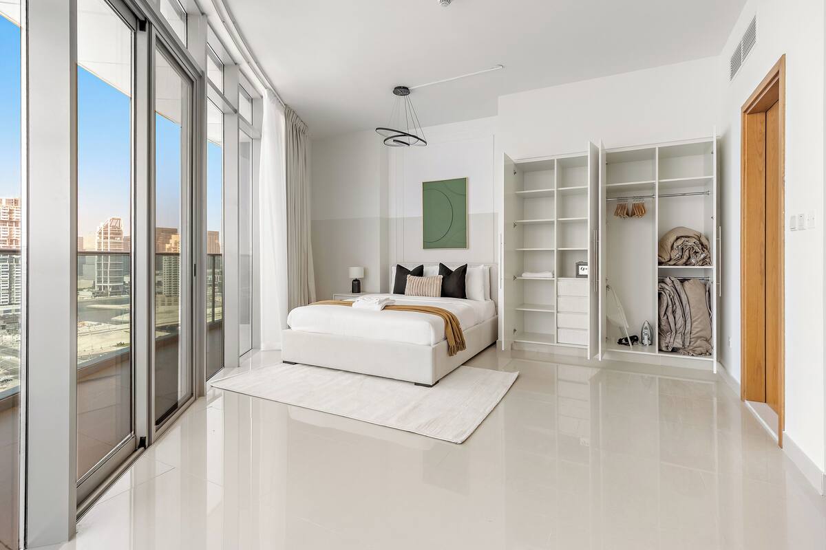 Une chambre moderne avec un grand lit, un dressing et une vue sur la ville.
