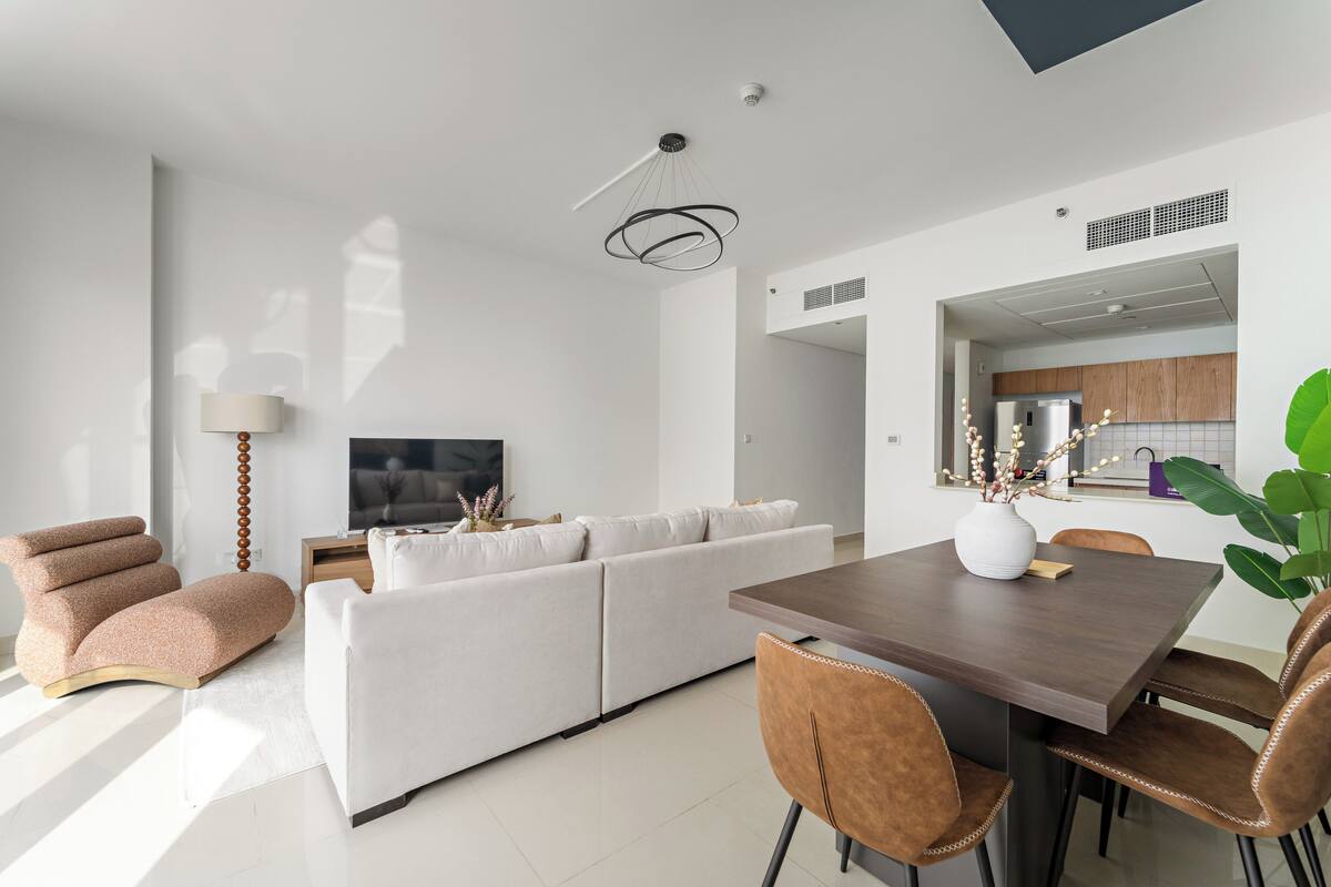 Un salon moderne avec un canapé, une table à manger et des chaises. On y trouve également un téléviseur, une lampe et une plante.