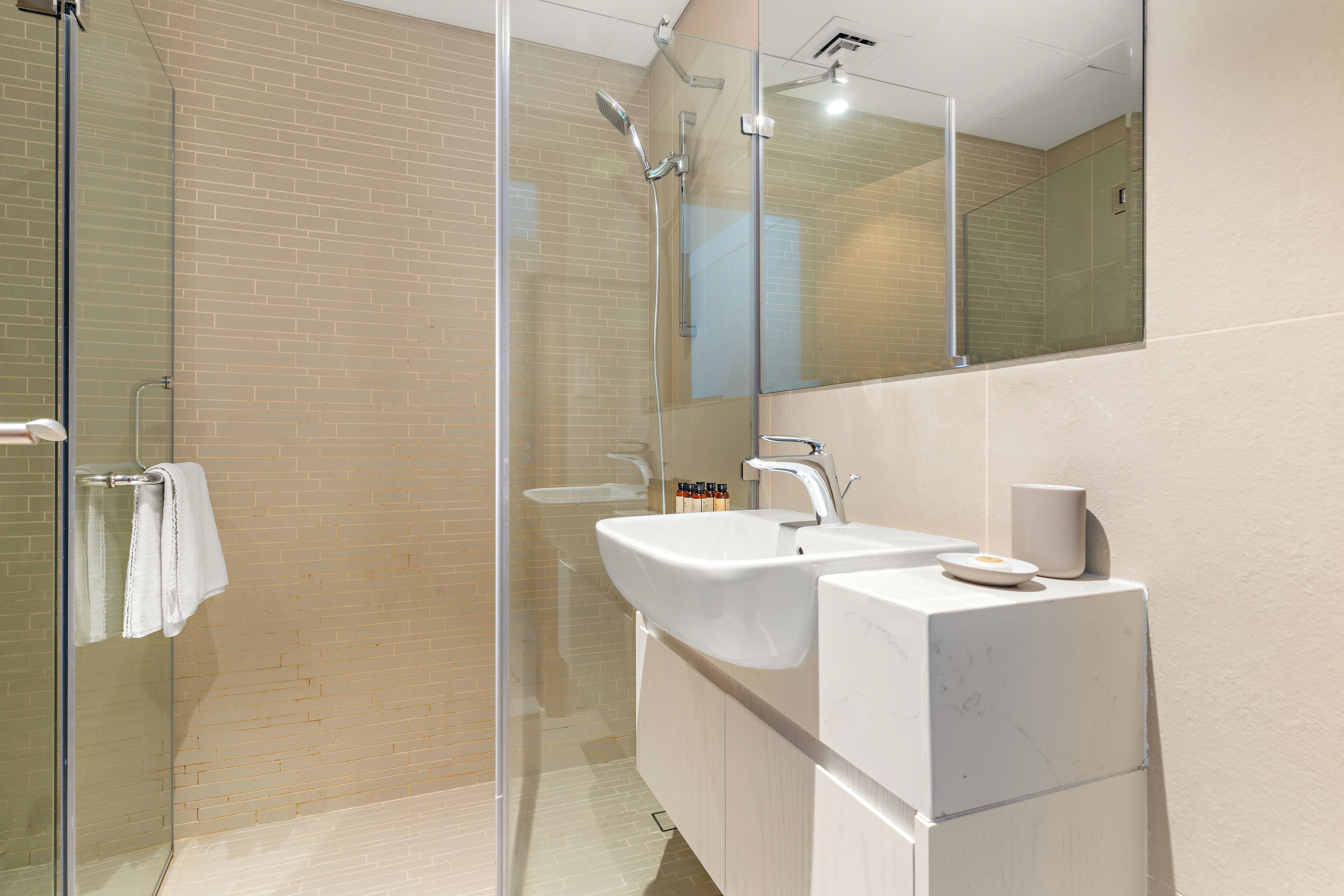 Une salle de bain moderne avec une douche à parois de verre, un lavabo blanc et un grand miroir.