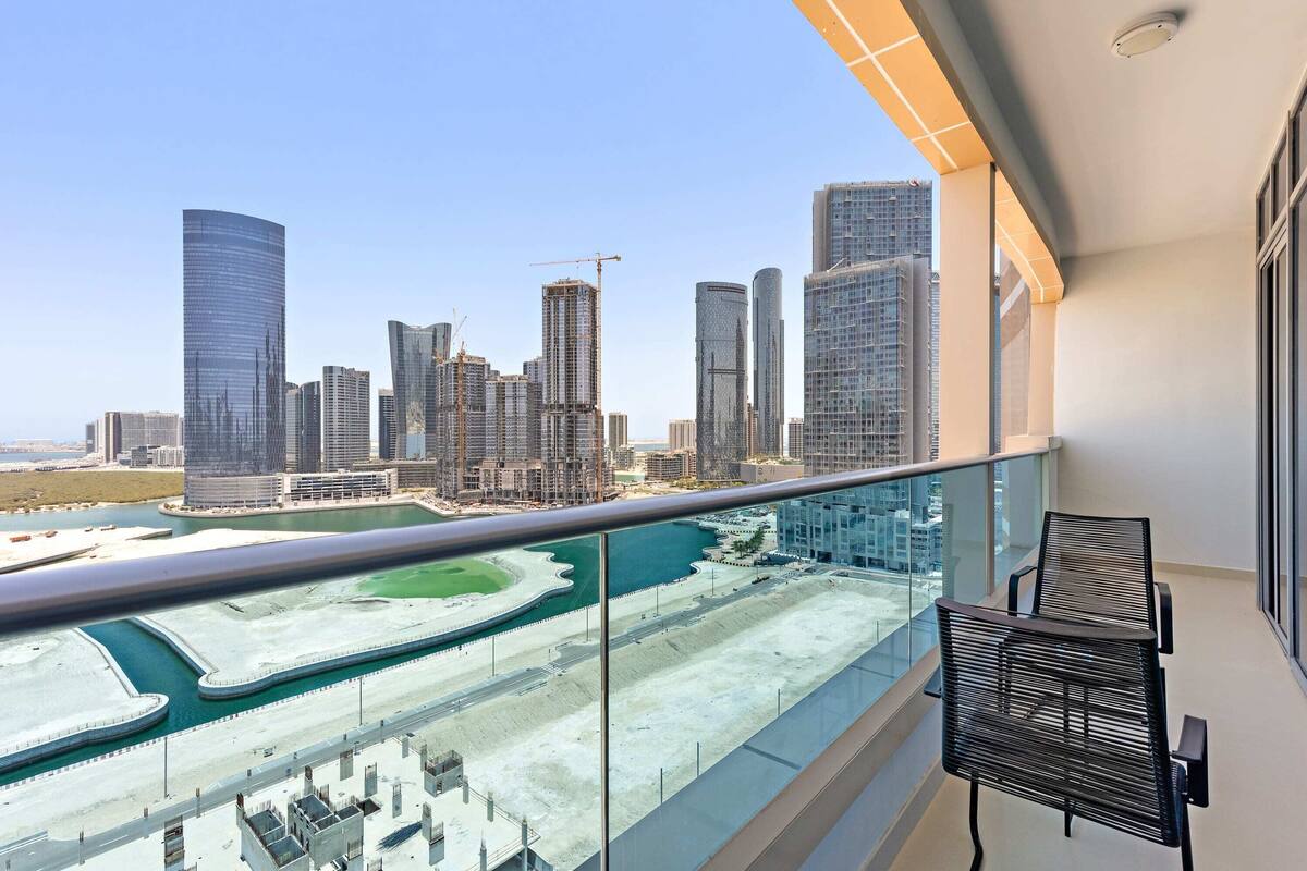 Un balcon offrant une vue sur les toits d’une ville, avec des immeubles de grande hauteur et un port de plaisance.