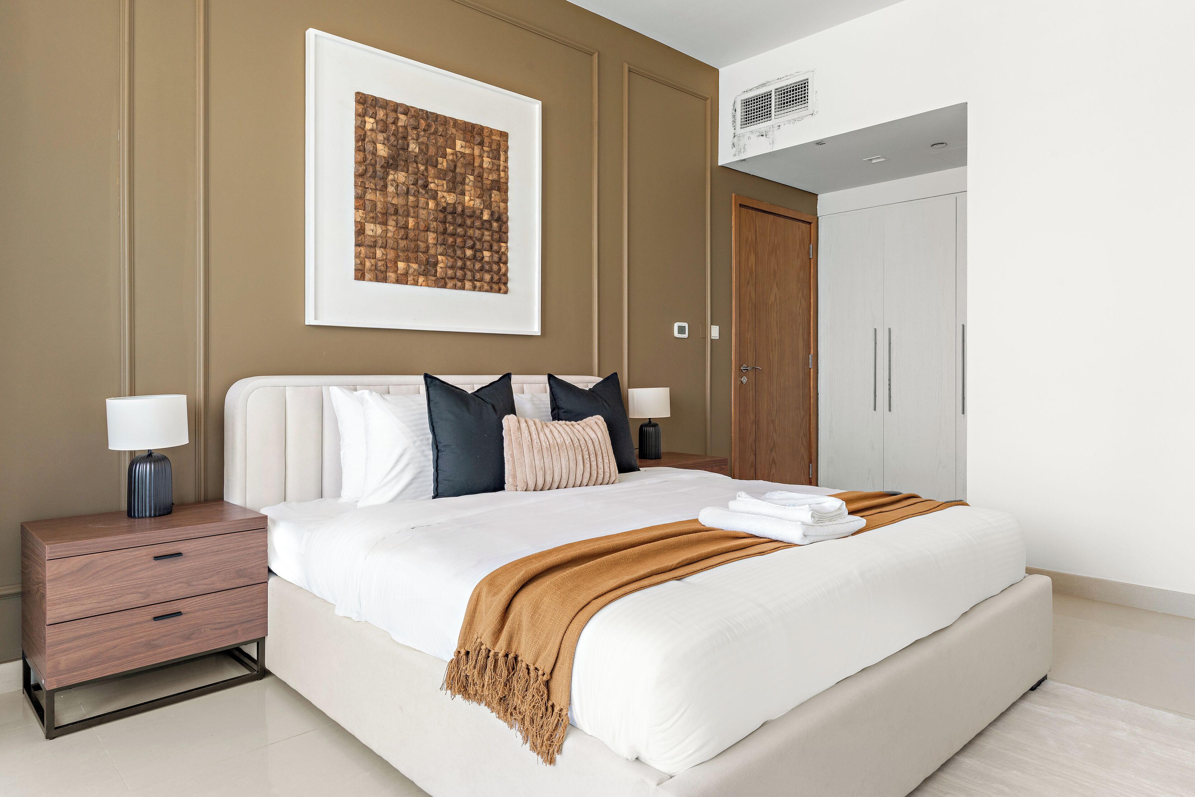 Een moderne slaapkamer met een groot bed, een nachtkastje, een lijst met kunstwerk aan de muur, en een kledingkast.