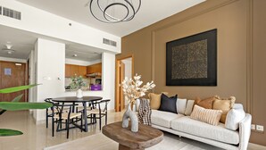 A modern living room with a wooden coffee table, a white sofa, and a dining area with a round table and chairs. - Silkhaus Julphar Tower, Al Reem Abu Dhabi (Abu Dhabi)