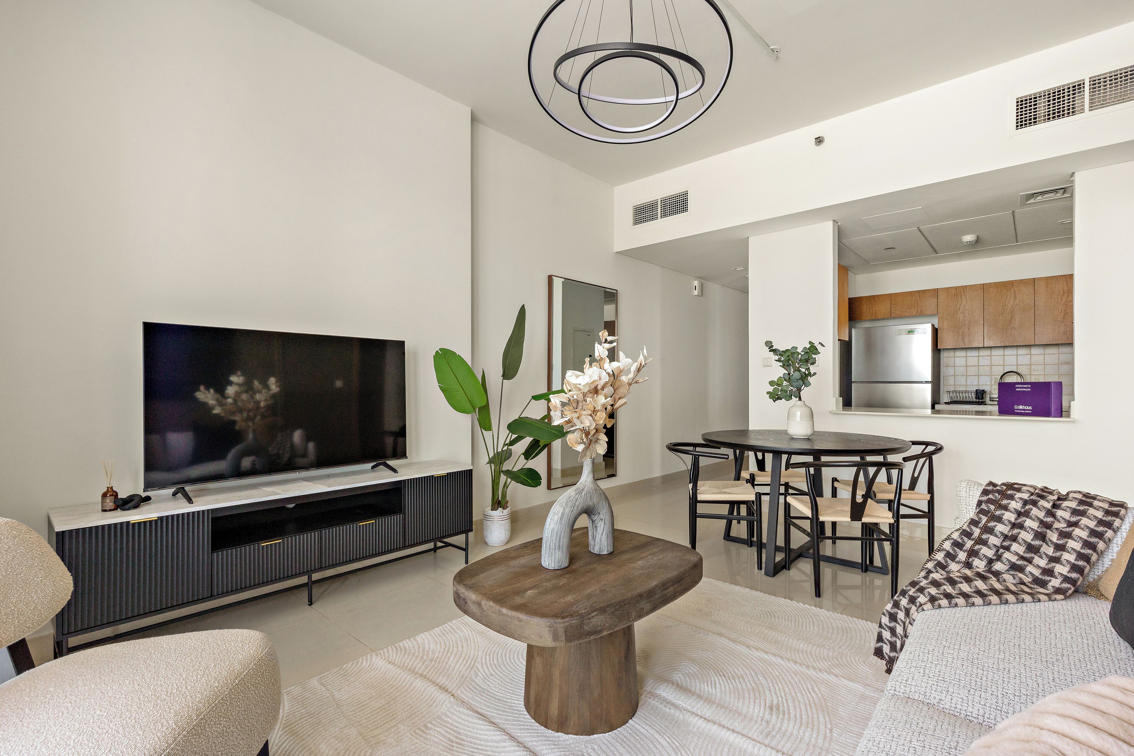 A modern living room with a flat-screen TV, a wooden coffee table, and a dining area with a table and chairs.