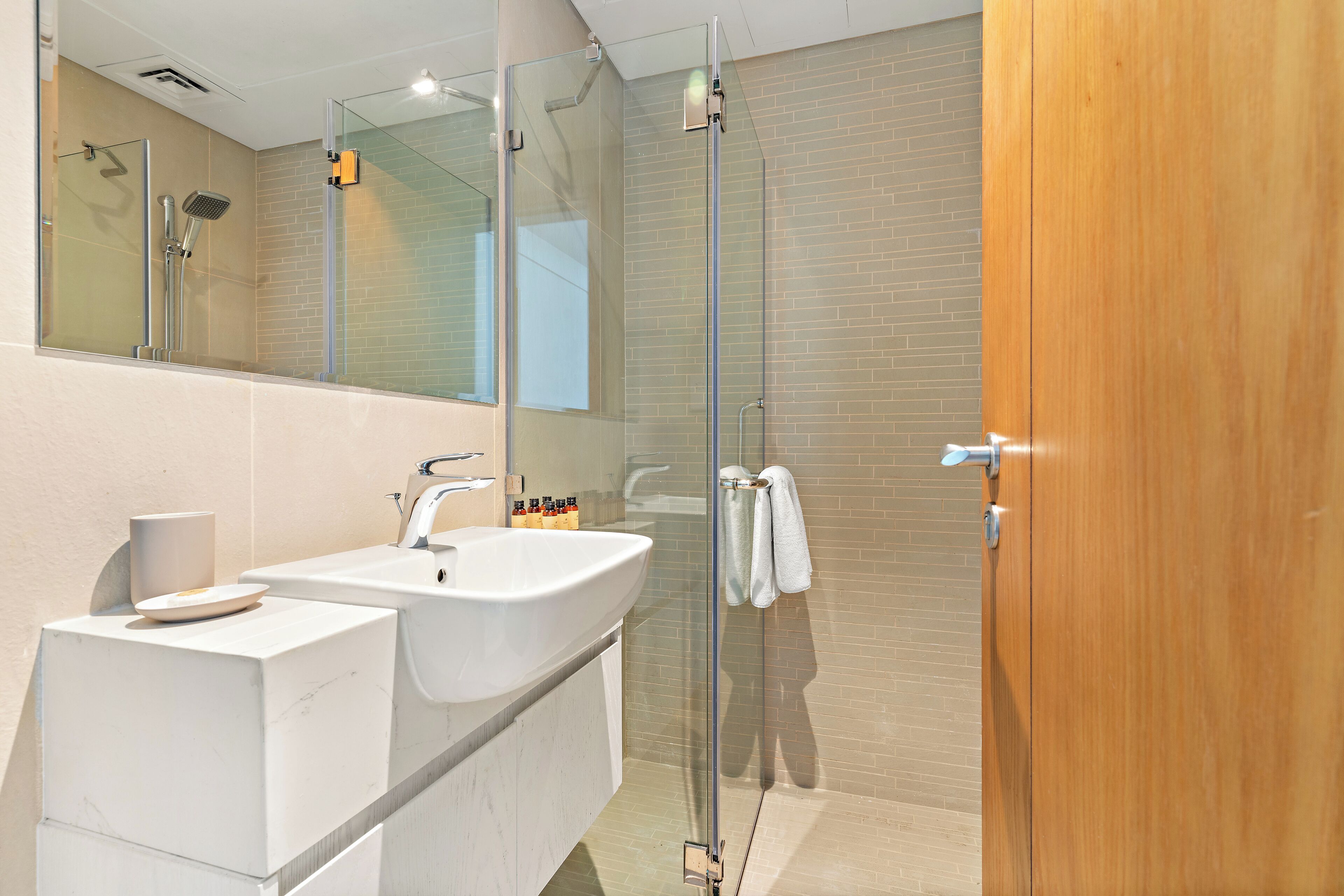A modern bathroom with a glass shower enclosure, two sinks, and a wooden door.