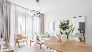 A modern living room with a round wooden dining table, white sofas, and a large window with sheer curtains. - Silkhaus Julphar Tower, Al Reem Abu Dhabi (Abu Dhabi)