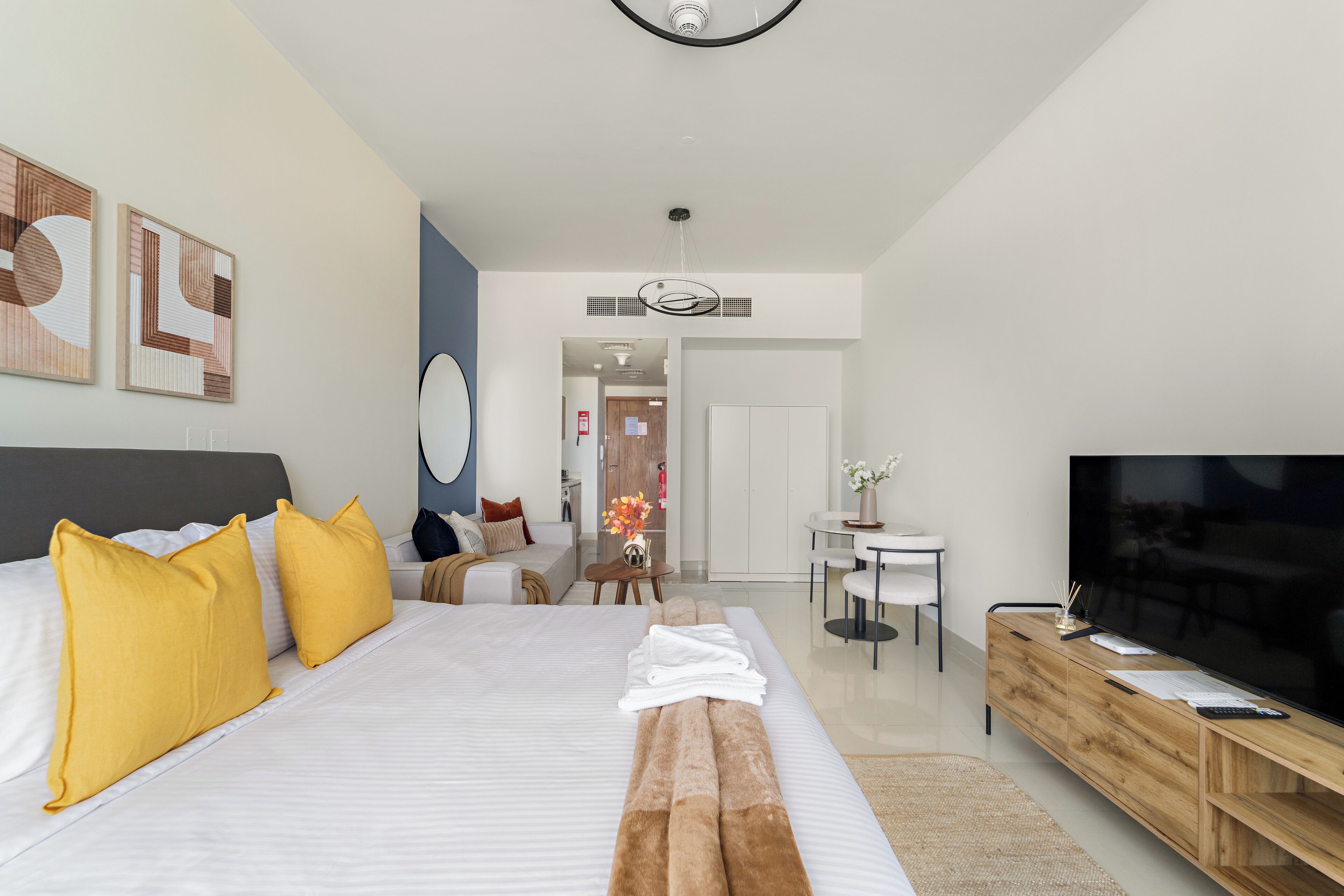A modern hotel room with a large bed, a TV, a wooden console, and a dining area.