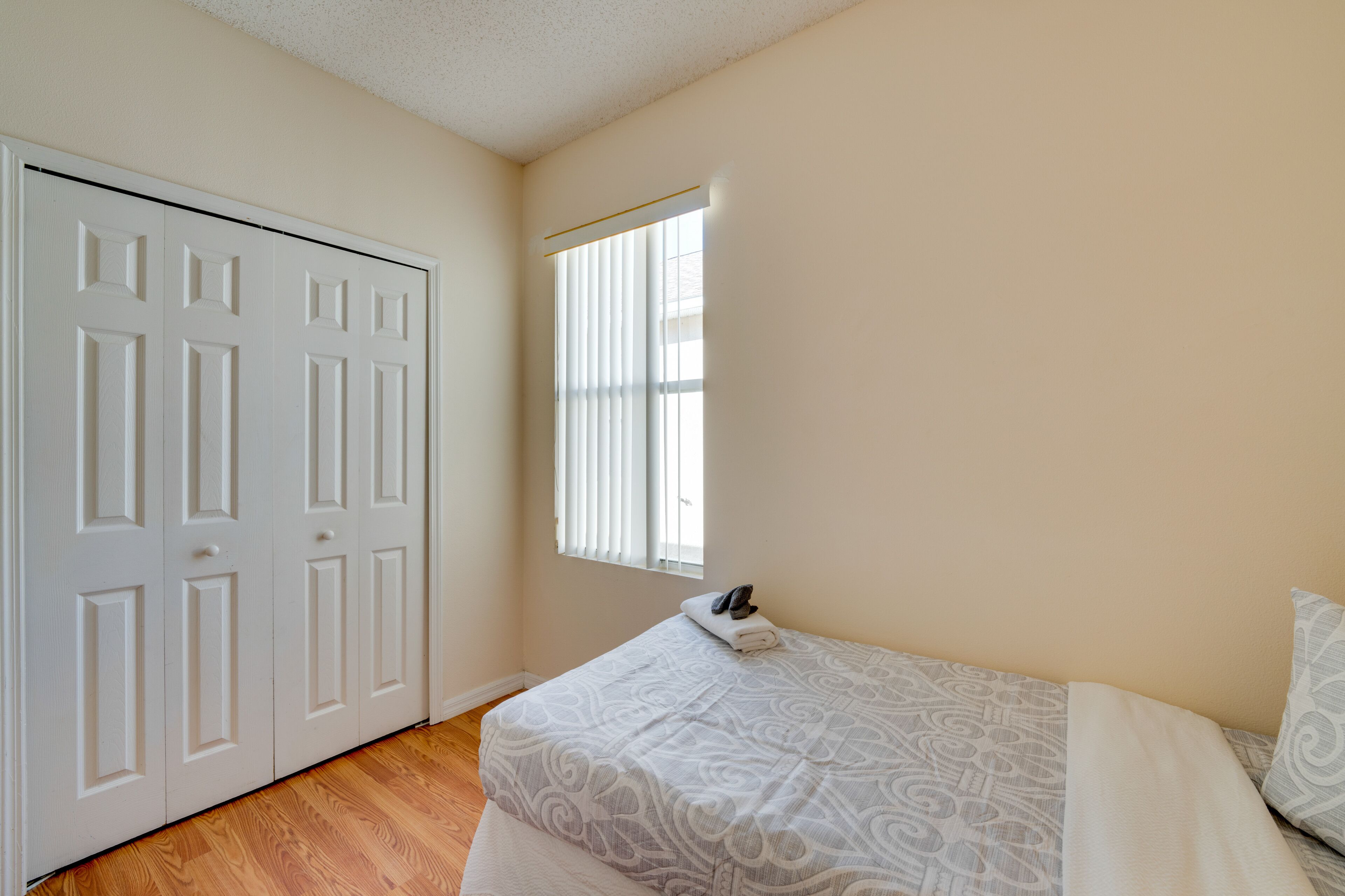 Une chambre à coucher avec un lit, une fenêtre avec des stores et une armoire blanche.