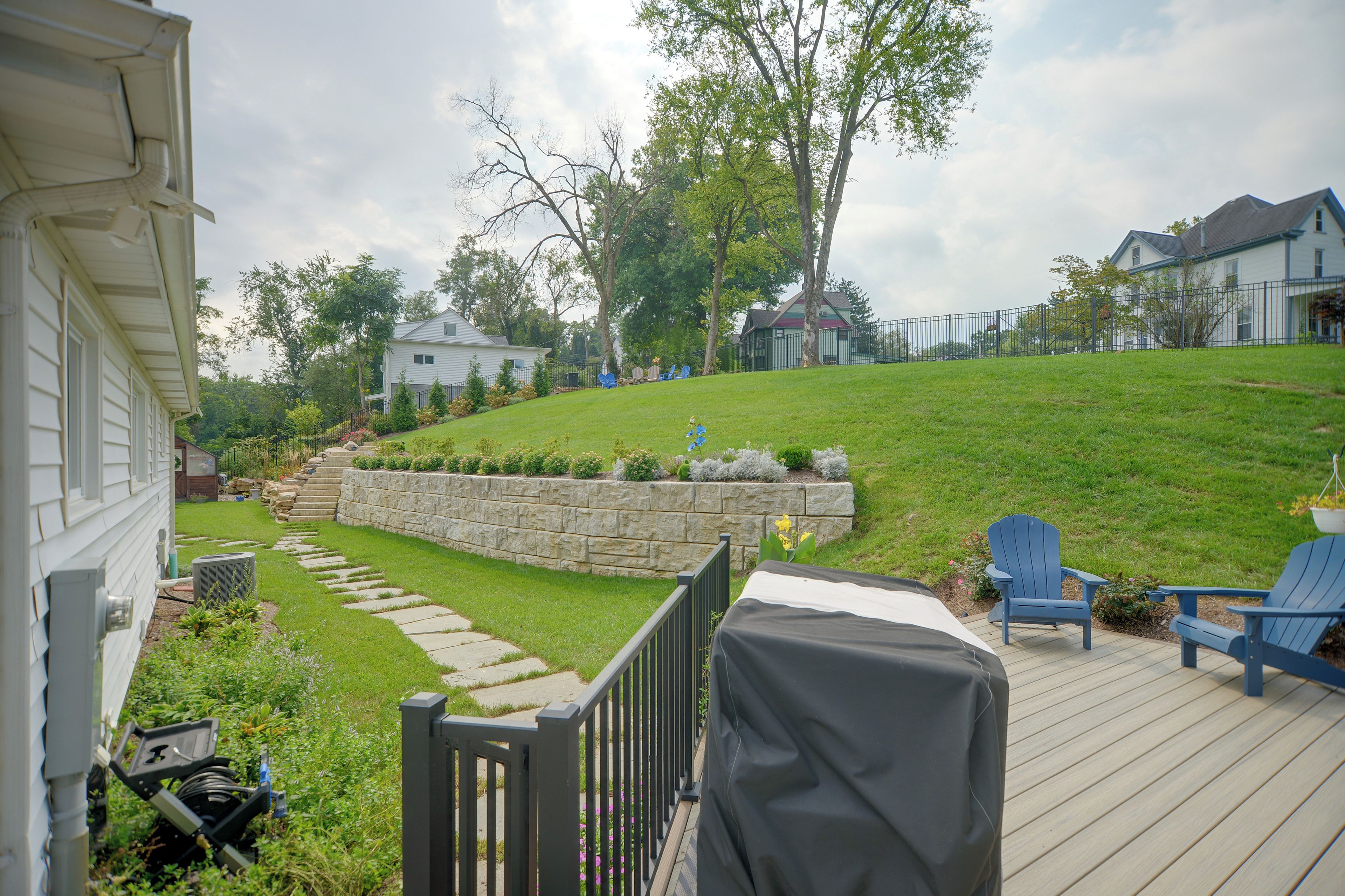 A backyard with a stone retaining wall, a wooden deck with Adirondack chairs, and a grassy lawn.