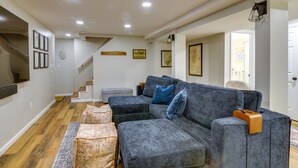 Un salon moderne avec un canapé d’angle gris, des poufs et un téléviseur à écran plat fixé au mur.