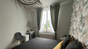A bedroom with a bed, a desk, a chair, and a window with curtains.