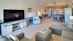 A living room with a large flat-screen TV, a sofa, ottoman, and a dining area with chairs and a table. - Pool Access & Balcony: Modern Myrtle Beach Condo (Myrtle Beach)