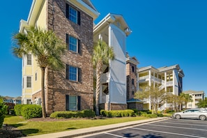 A multi-story building with a brick facade, balconies, and a parking lot.