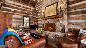 L’intérieur d’une cabane en rondins, avec des meubles en cuir, une cheminée en pierre et une carte accrochée au mur.