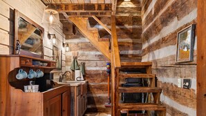 Un intérieur rustique avec des murs en bois, un escalier en bois, un coin cuisine doté d’un évier et de placards, et un luminaire suspendu.