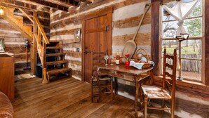 L’intérieur d’un chalet rustique en bois, avec un escalier en bois, une table à manger entourée de chaises et une fenêtre agrémentée d’un rideau.